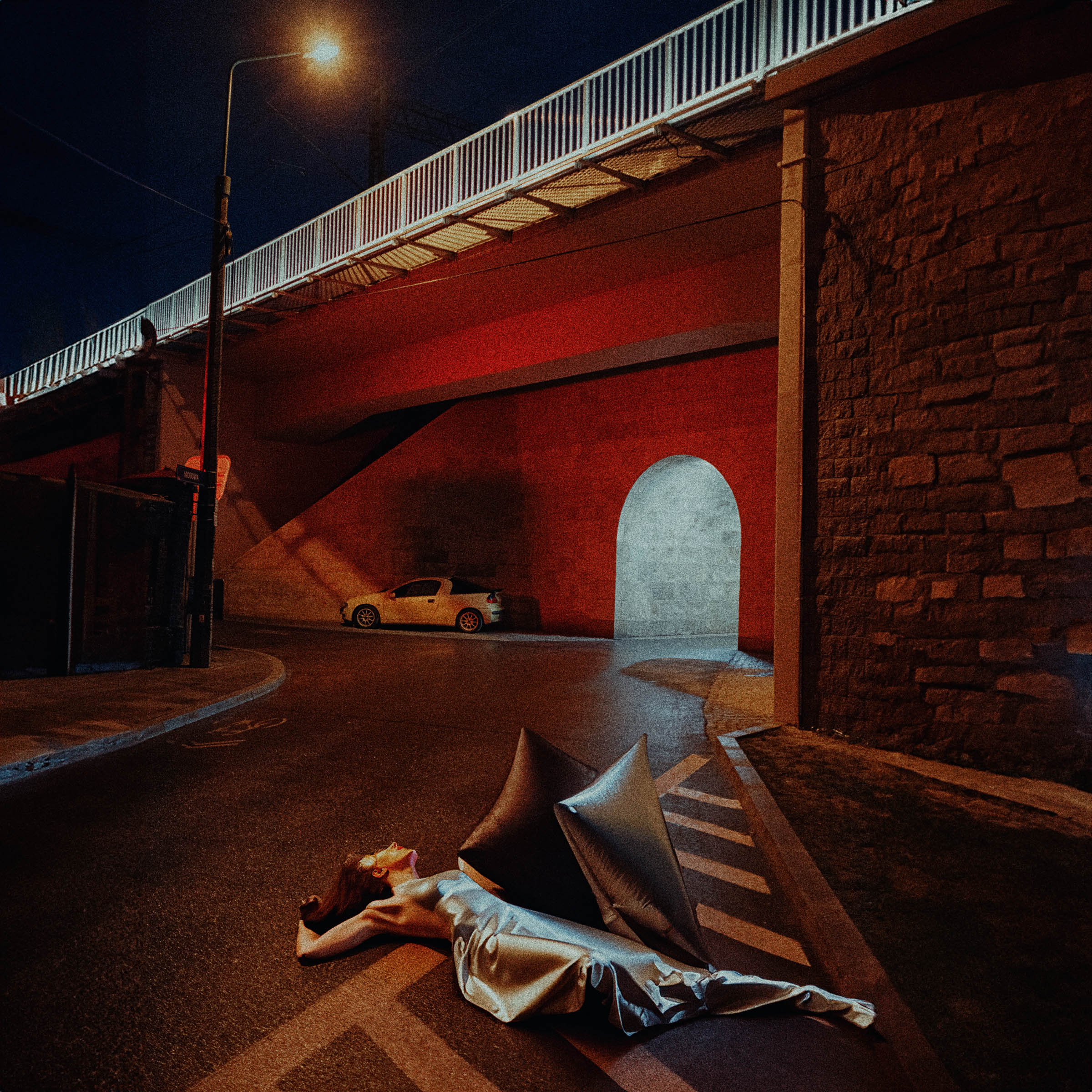Nocna scena pod mostem, oświetlony tunel i postać na jezdni.